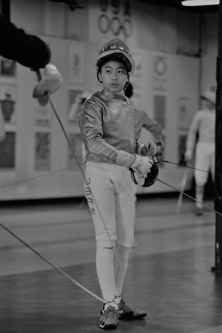 a black and white photo of a young fencern private lesson with full feancing gear on with saber in hand