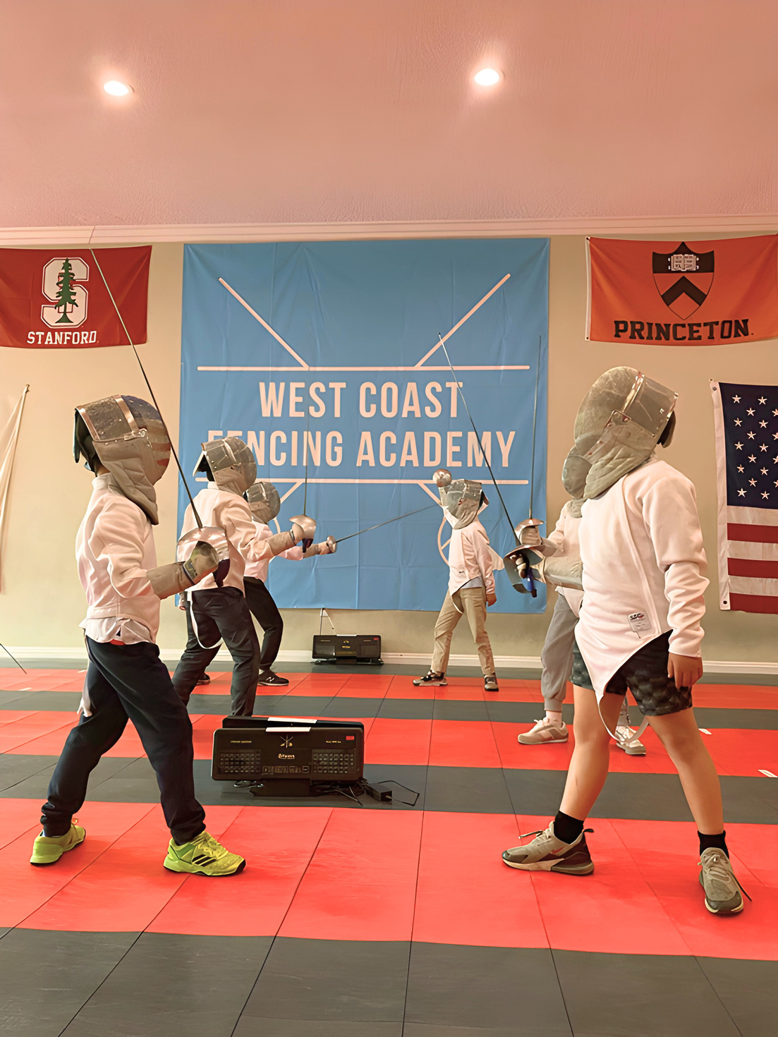 A group of young saber fencing in saber fencing gear with mask, gloves and saber practicing saber fencing drills at West Coast Fencing Academy in the Advance Youth Class.