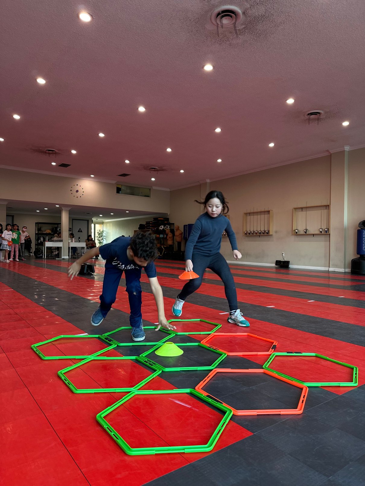 two children playing with a game of hexagons on a gym floor. they are participate in saber fencing agility and conditioning drills to improve their reaction time. 