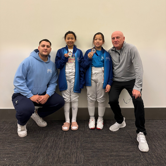 Coach Gherman stone and Coach Mike Kishchenkov posing with two Y12 girls after they won top 8 medals at regional saber fencing tournament in California