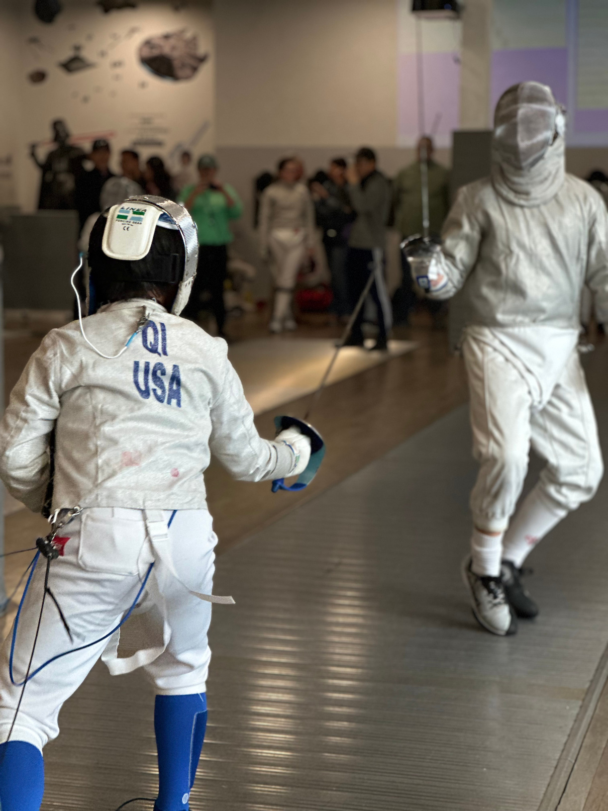 Two Boy saber fencers in fencing gear at a local tournament in Southern California on a metal fencing strip