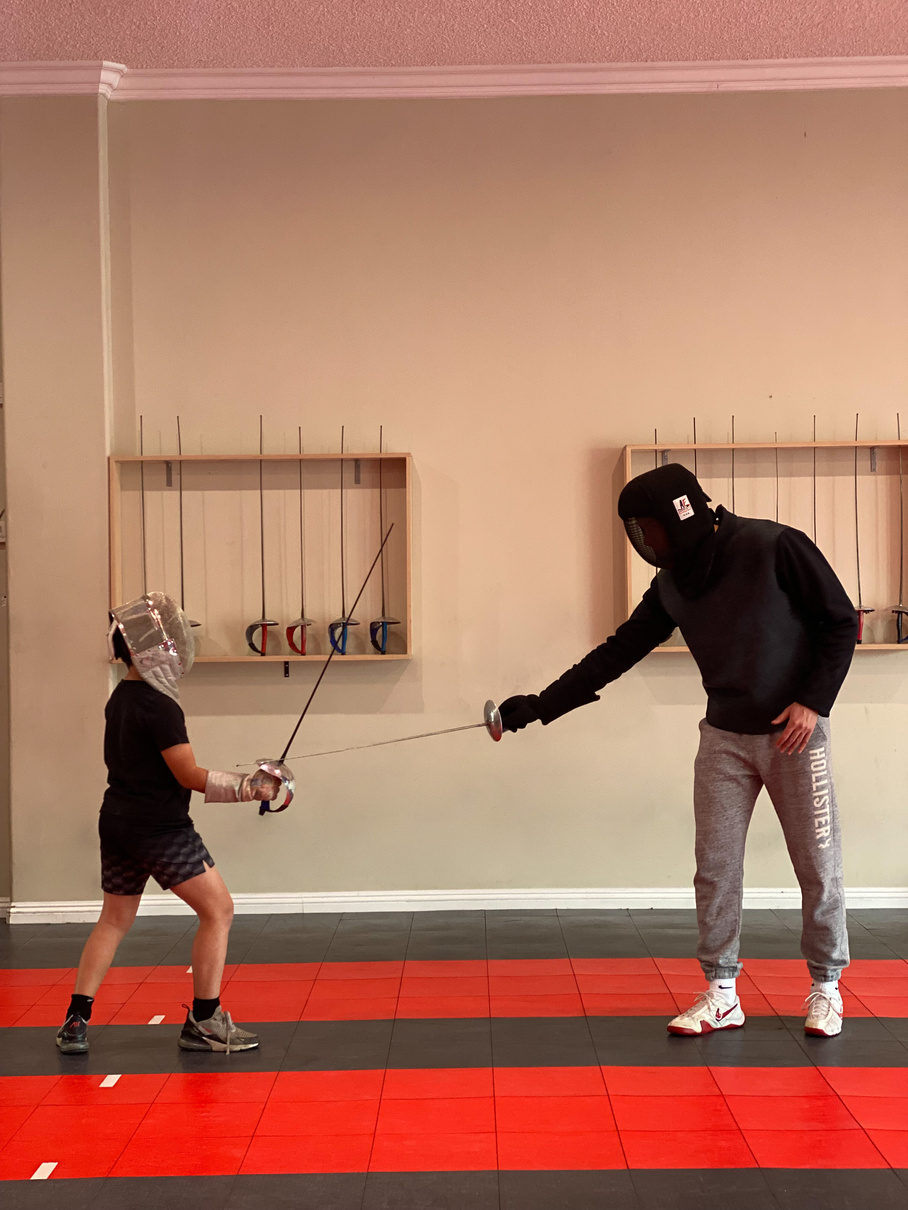 Coach Artem having a saber private lesson with a young boy with fencing mask and saber in hand practicing bladework