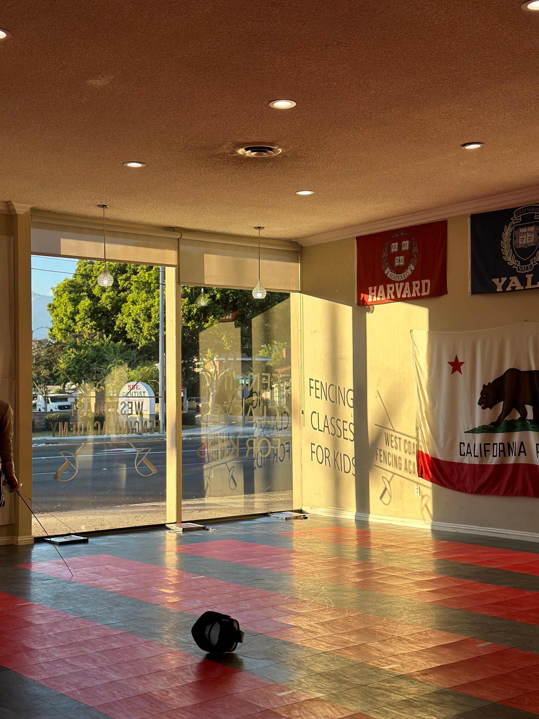 a person standing in front of a california flag with the sign fencing classes for kids at West Coast Fencing Academy with fencing strips in sight. 