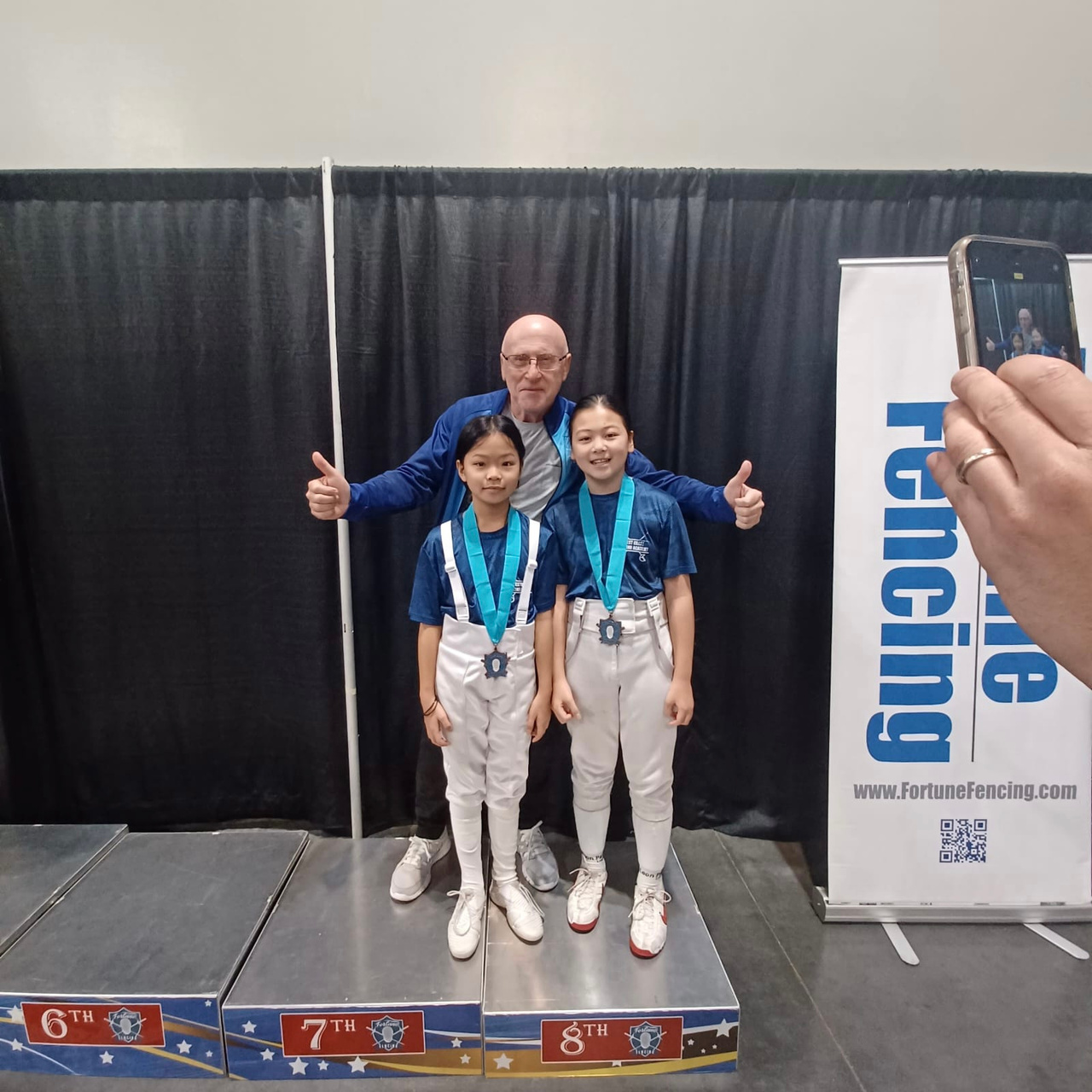 coach gherman stone behind two young girl fencers who won medals at their fencing tournament