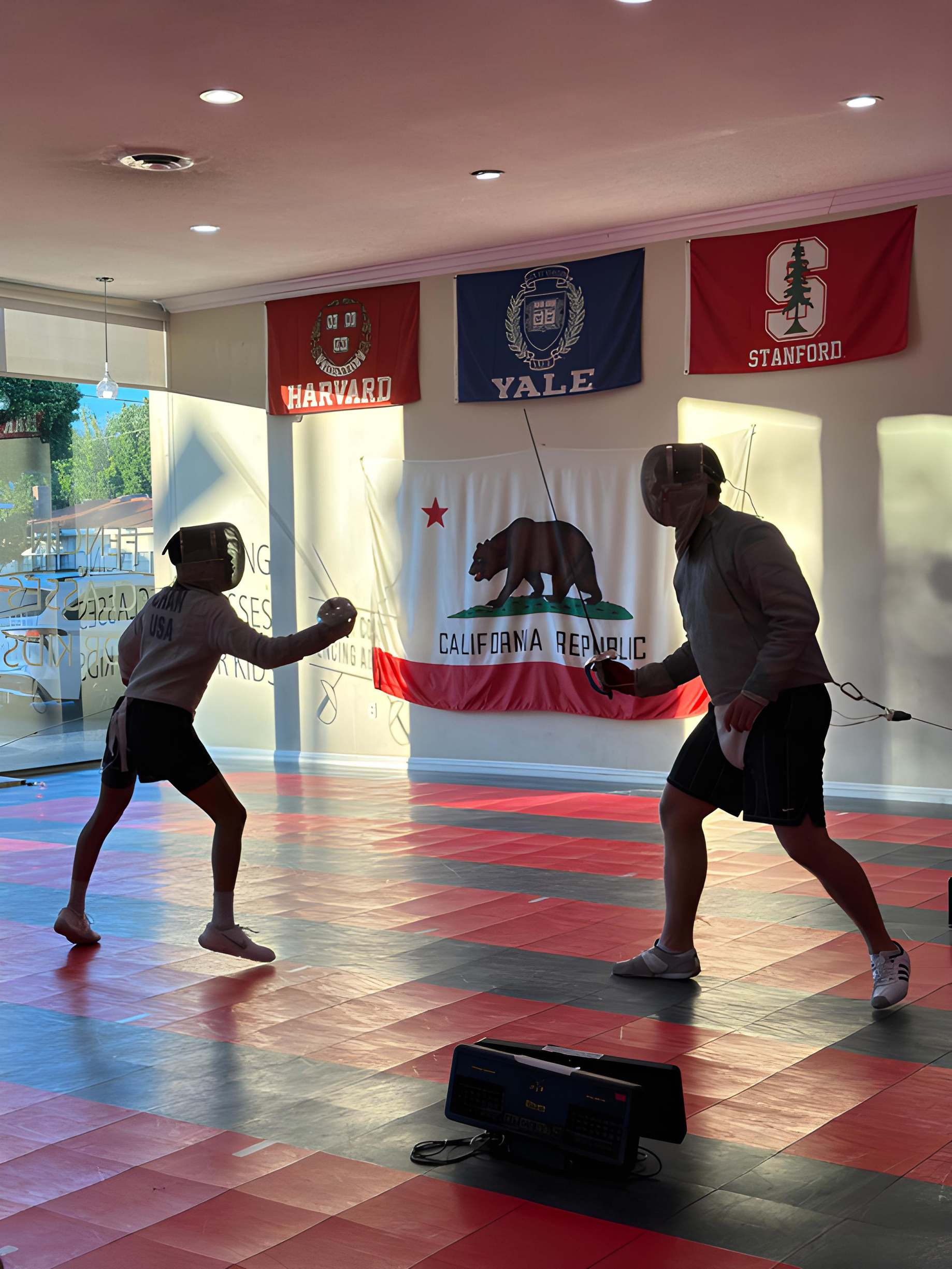 two people are practicing saber fencing in a room with a california flag on the wall