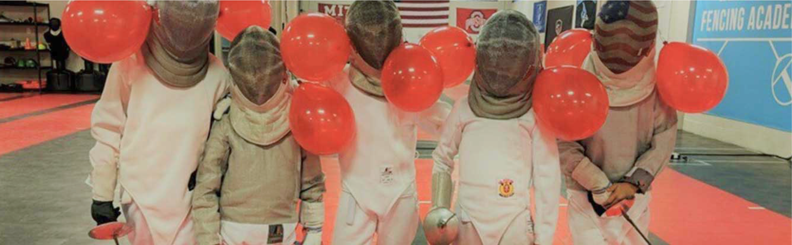 a row of kids saber fencers at a birthday party at West Coast fencing academy in full saber fencing gear with red balloons