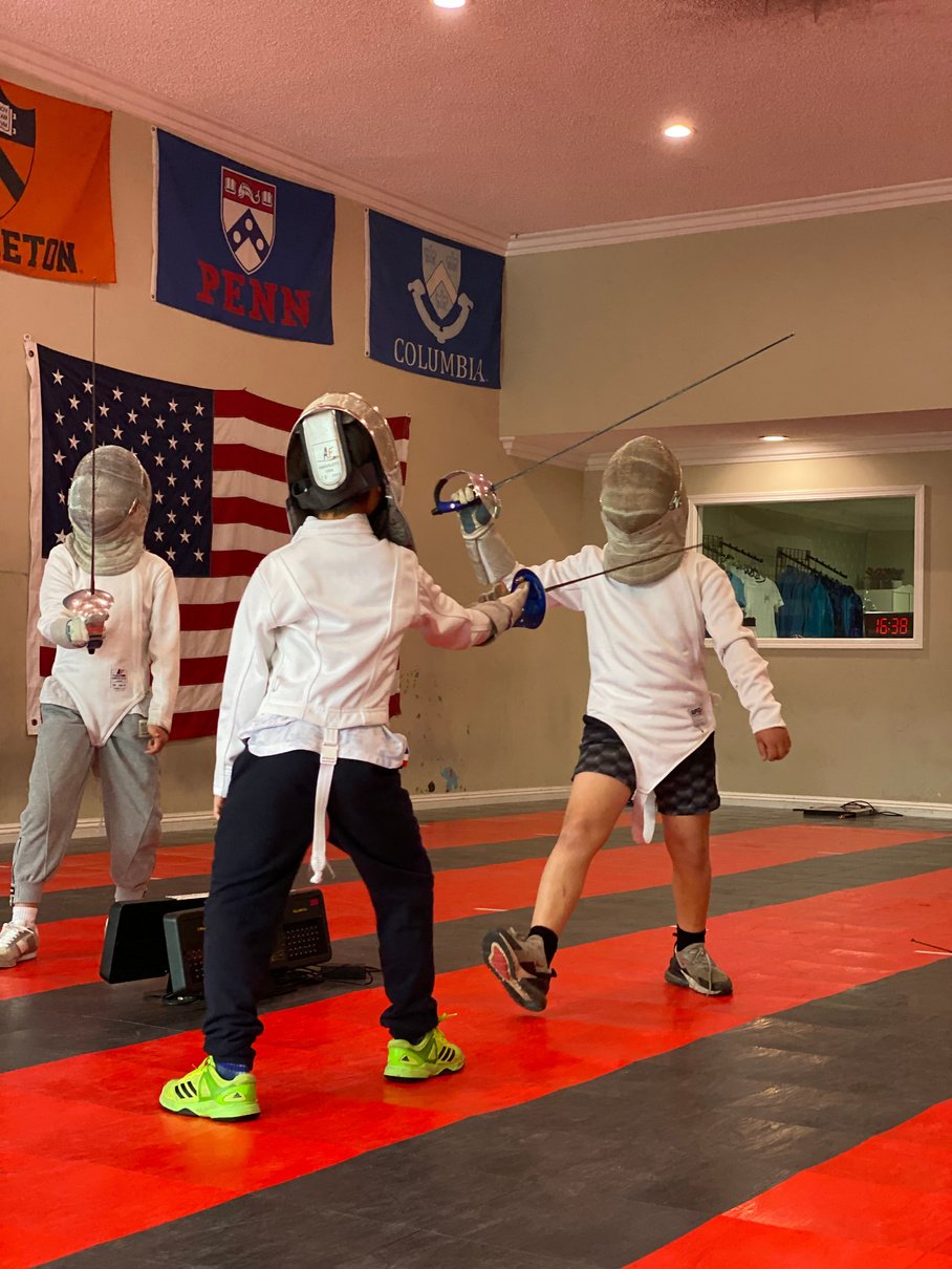 a group of young kids wearing non electric saber fencing gear practicing saber fencing drills