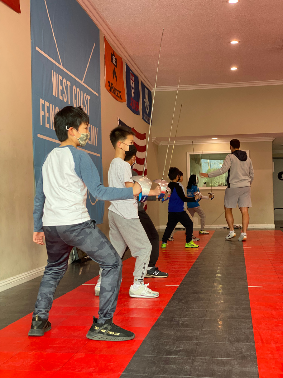 a group of kids with saber in hand practicing saber fencing footwork